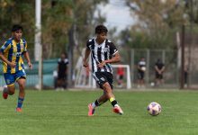 Jogadores adolescentes disputam uma partida de futebol em um campo gramado ao ar livre.