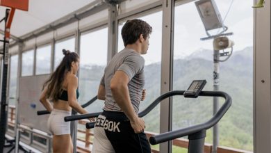 Duas pessoas correm em esteiras lado a lado em uma academia com vista para montanhas.