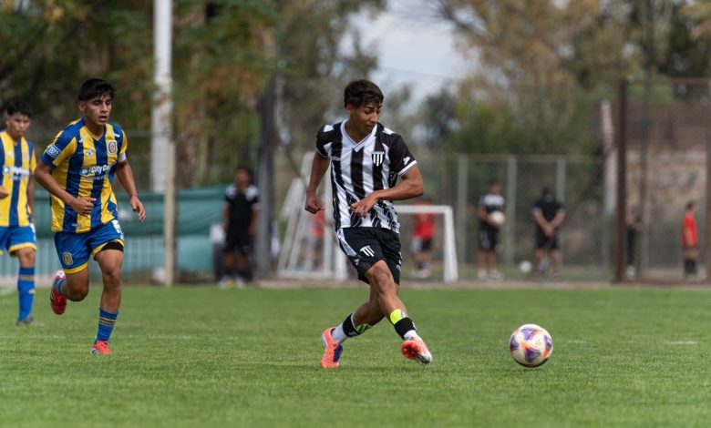 Jogadores adolescentes disputam uma partida de futebol em um campo gramado ao ar livre.