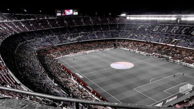 Vista aérea de um grande estádio de futebol contemporâneo, com torcedores nas arquibancadas e o campo iluminado.