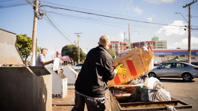 Dois trabalhadores realizam atividade de coleta e descarte de resíduos em uma área urbana ensolarada.