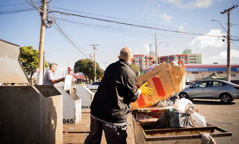 Dois trabalhadores realizam atividade de coleta e descarte de resíduos em uma área urbana ensolarada.