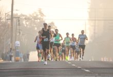 Grupo de corredores participa de uma maratona em uma rua arborizada durante uma manhã de neblina.